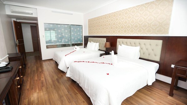 Habitación de hotel con dos camas, suelo de madera, un ventanal grande y un papel tapiz estampado.