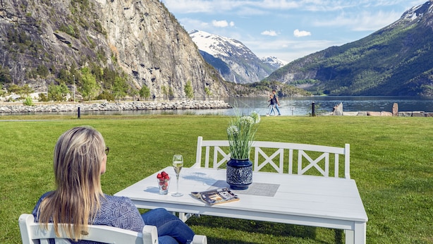 A person seated at a white table with a view of a lake and mountains. - Valldal Fjordhotell - by Classic Norway Hotels (Fjord)