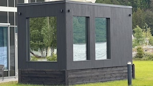A modern, dark-colored outdoor structure with large windows, situated in a grassy area with a lake view. - Valldal Fjordhotell - by Classic Norway Hotels (Fjord)