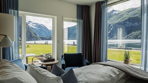 A hotel room with a bed, a chair, a small table, and a view of a lake and mountains. - Valldal Fjordhotell - by Classic Norway Hotels (Fjord)
