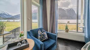 A room with a view of mountains and a lake, a blue sofa, and a tray with glasses and a flower. - Valldal Fjordhotell - by Classic Norway Hotels (Fjord)