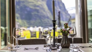 A dining table set with wine glasses, a candle, and a vase with flowers, overlooking a mountainous landscape. - Valldal Fjordhotell - by Classic Norway Hotels (Fjord)