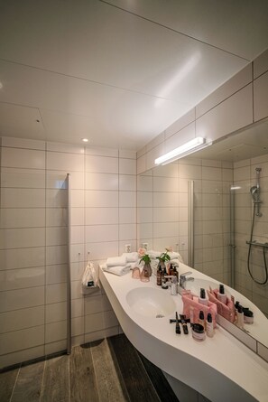 A modern bathroom with a large mirror, white tiles, a shower, and a vanity with toiletries. - Valldal Fjordhotell - by Classic Norway Hotels (Fjord)