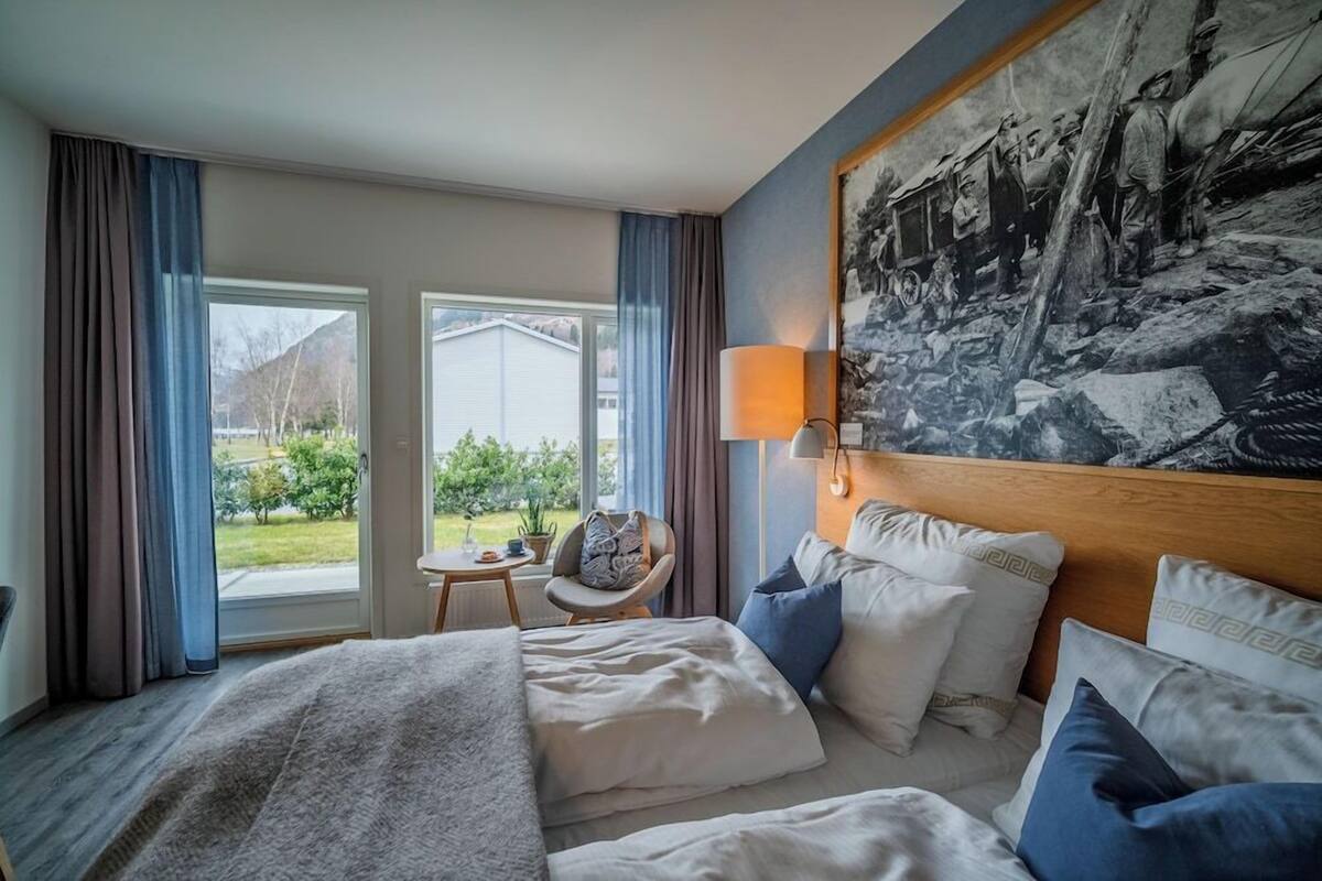 Ein Hotelzimmer mit Bett, Sessel, Tisch und einem großen Fenster.