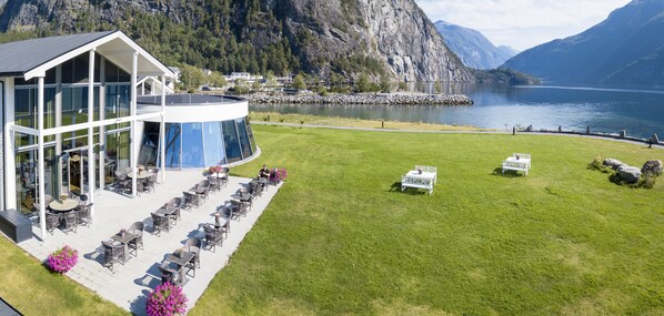 A modern building with a glass facade and outdoor seating area with tables and chairs. - Valldal Fjordhotell - by Classic Norway Hotels (Fjord)