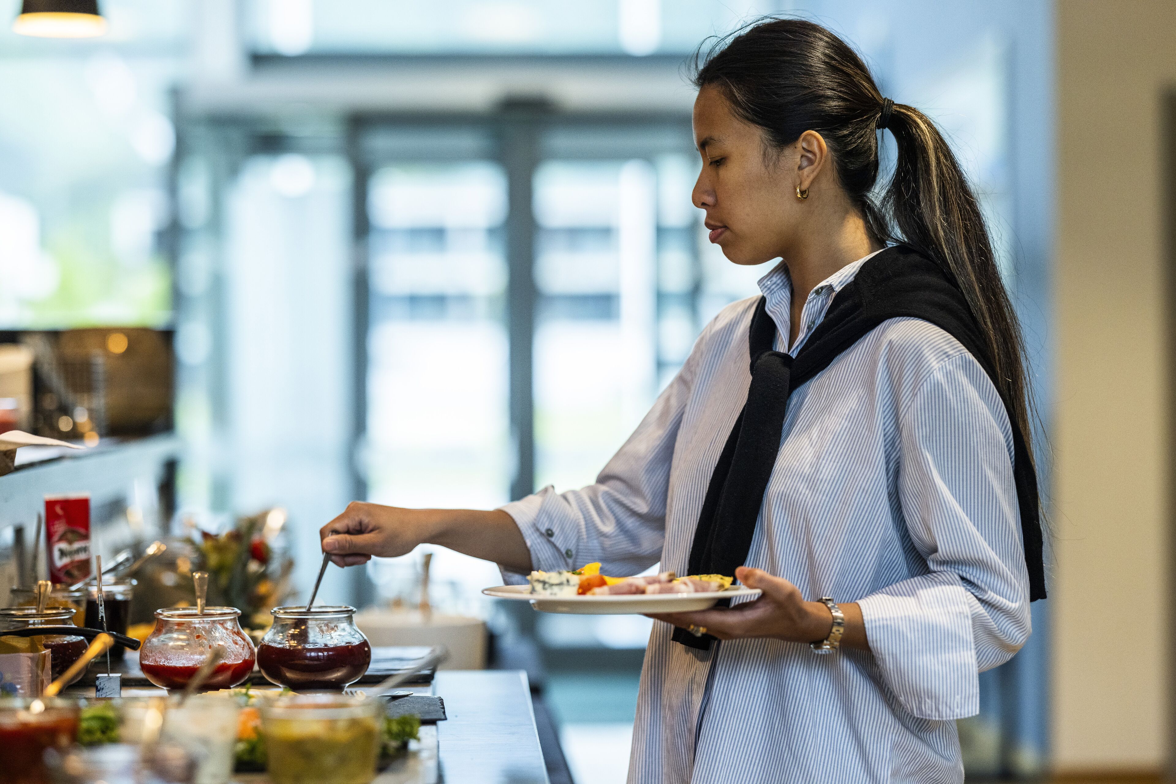 A person serving food at a buffet with various dishes and condiments.