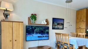 A modern living room with a flat-screen TV, wooden furniture, and a dining area. - N 7 (BC.a5) - Stranddomicil Steiner (Büsum)