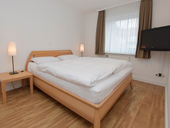 A neatly made bed with white linens, a wooden headboard, and a nightstand with a lamp.