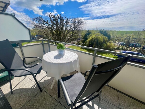 A balcony with a round table, two chairs, and a potted plant.