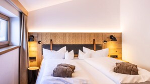 Quarto de hotel com cabeceira de madeira, cama grande com roupa de cama branca, duas luminárias de cabeceira e uma janela com cortinas.