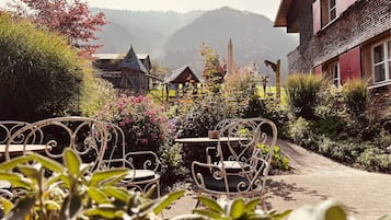 A garden with metal chairs and tables, a wooden structure, and a mountain backdrop.