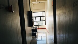 A long, narrow hallway with a reflective floor, leading to a room with a large window and a chair. - Heart Hotel and Services (Dumaguete)