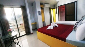 A hotel room with a bed, a small table with a chair, a balcony with curtains, and a window. - Heart Hotel and Services (Dumaguete)