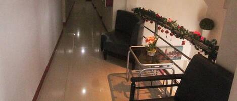 Um hall de hotel com um corredor comprido, escada e área de estar com mesa e cadeiras.