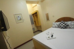 Habitación de hotel con cama, mesita de noche con control remoto y teléfono, armario y un cuadro en la pared.