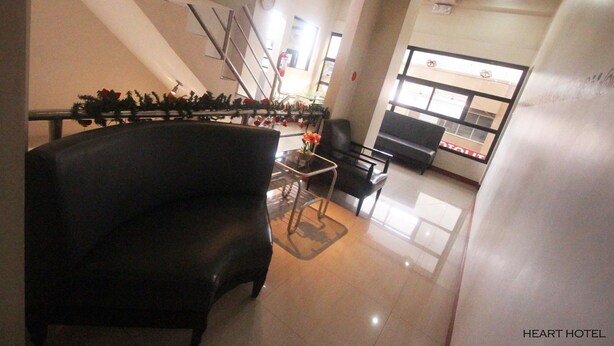 A hotel lobby with a black leather sofa, a small table with a vase of flowers, and a reception desk. - Heart Hotel and Services (Dumaguete)