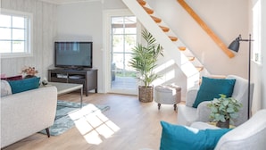 Sala de estar moderna com televisão, sofá, poltrona, escada de madeira e janelas amplas.