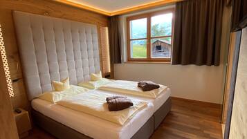 A double bed with a tufted headboard, two pillows, and a window with a view of a wooden cabin.