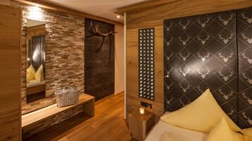 Een moderne kamer met een houten vloer, een bed met gele kussens, een bankje met een mand, een spiegel en een muur met een hertenpatroon.
