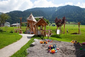 A playground with a wooden play structure, a dirt play area with toys, and a path leading to it. - Postsuite - Alpen Hotel Post **** (Au)