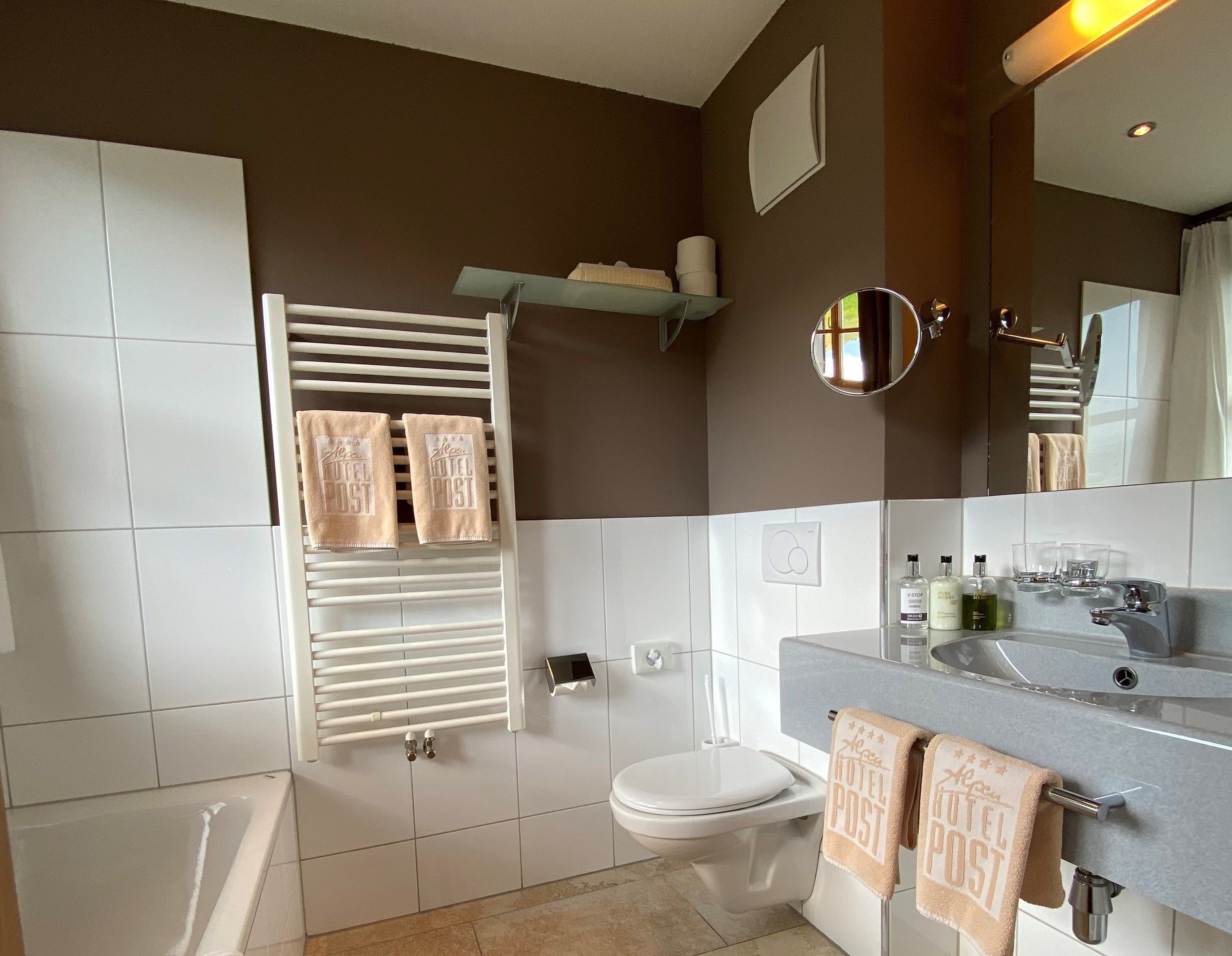 Un bagno moderno con vasca, servizi igienici e lavandino, con asciugamani che presentano il marchio 'Hotel Post'.
