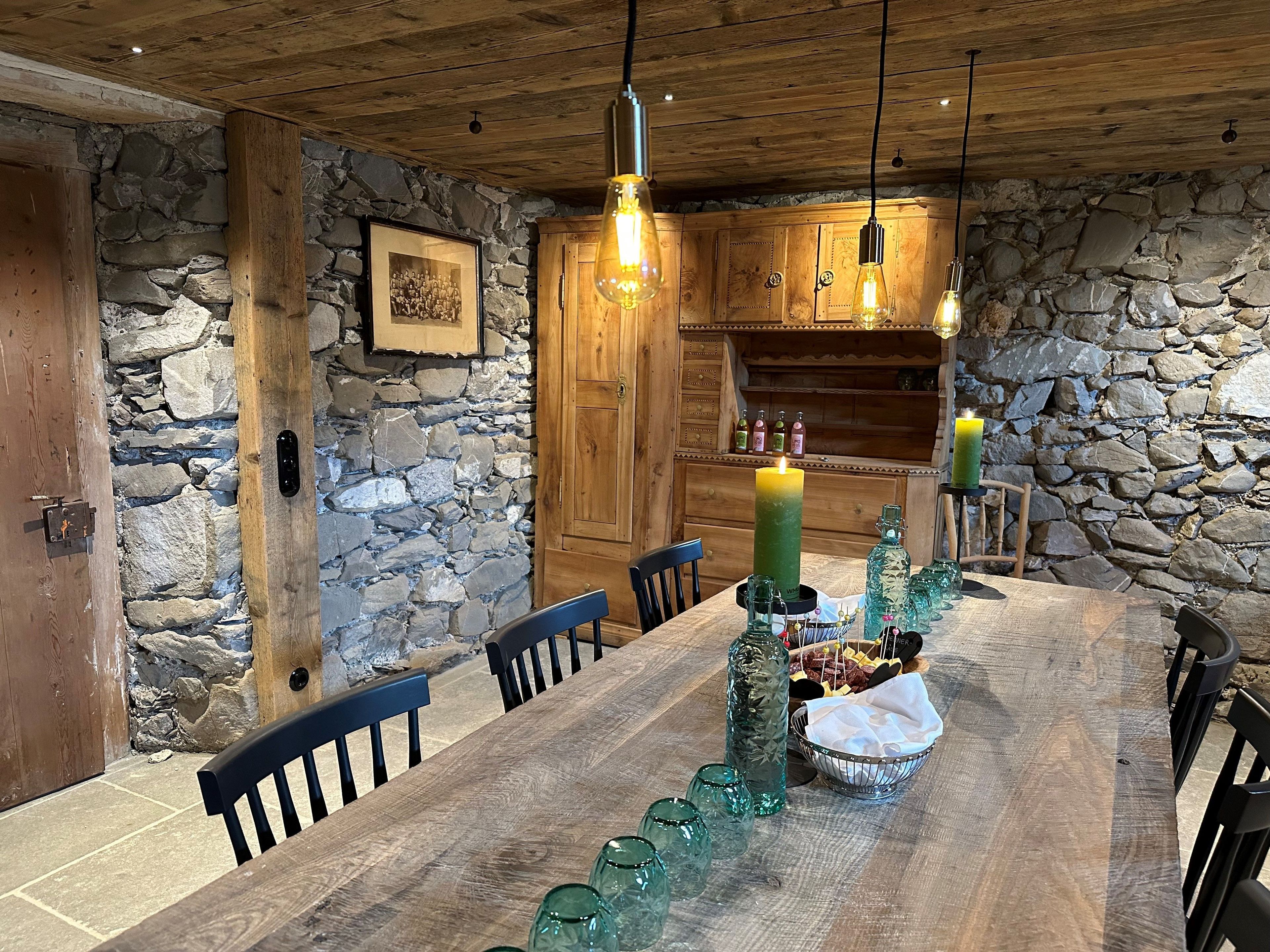 A rustic dining area with a wooden table, stone walls, and hanging light fixtures.