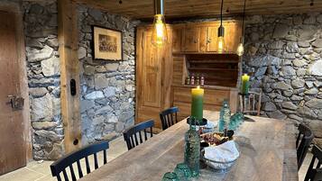 A rustic dining area with a wooden table, stone walls, and hanging light fixtures.