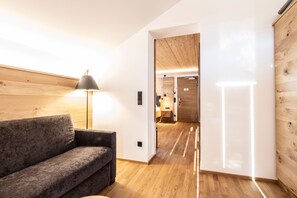 A modern interior with a wooden floor, a grey sofa, and a lamp. - Postsuite - Alpen Hotel Post **** (Au)