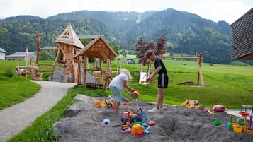 Ein Spielplatz mit Sandbereich, Holzspielgeräten und einer malerischen Bergkulisse.