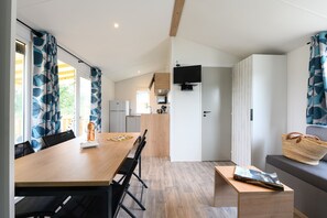 A modern kitchen with a built-in microwave, a wooden dining table with chairs, and a bench with a woven bag. - Camping le Paradis (Talmont-Saint-Hilaire)