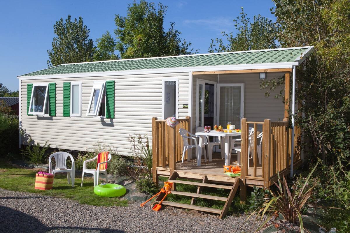 A mobile home with a deck, outdoor seating, and a small garden area.