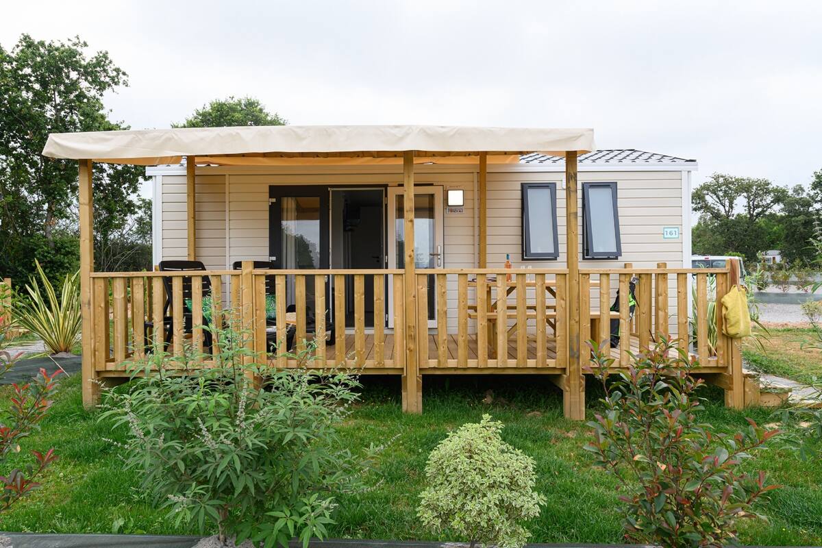 A mobile home with a covered porch, a small deck, and a number '161' on the side.