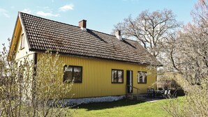 Une maison en bois jaune, avec un toit en tuiles, une cheminée et un petit porche doté de chaises.