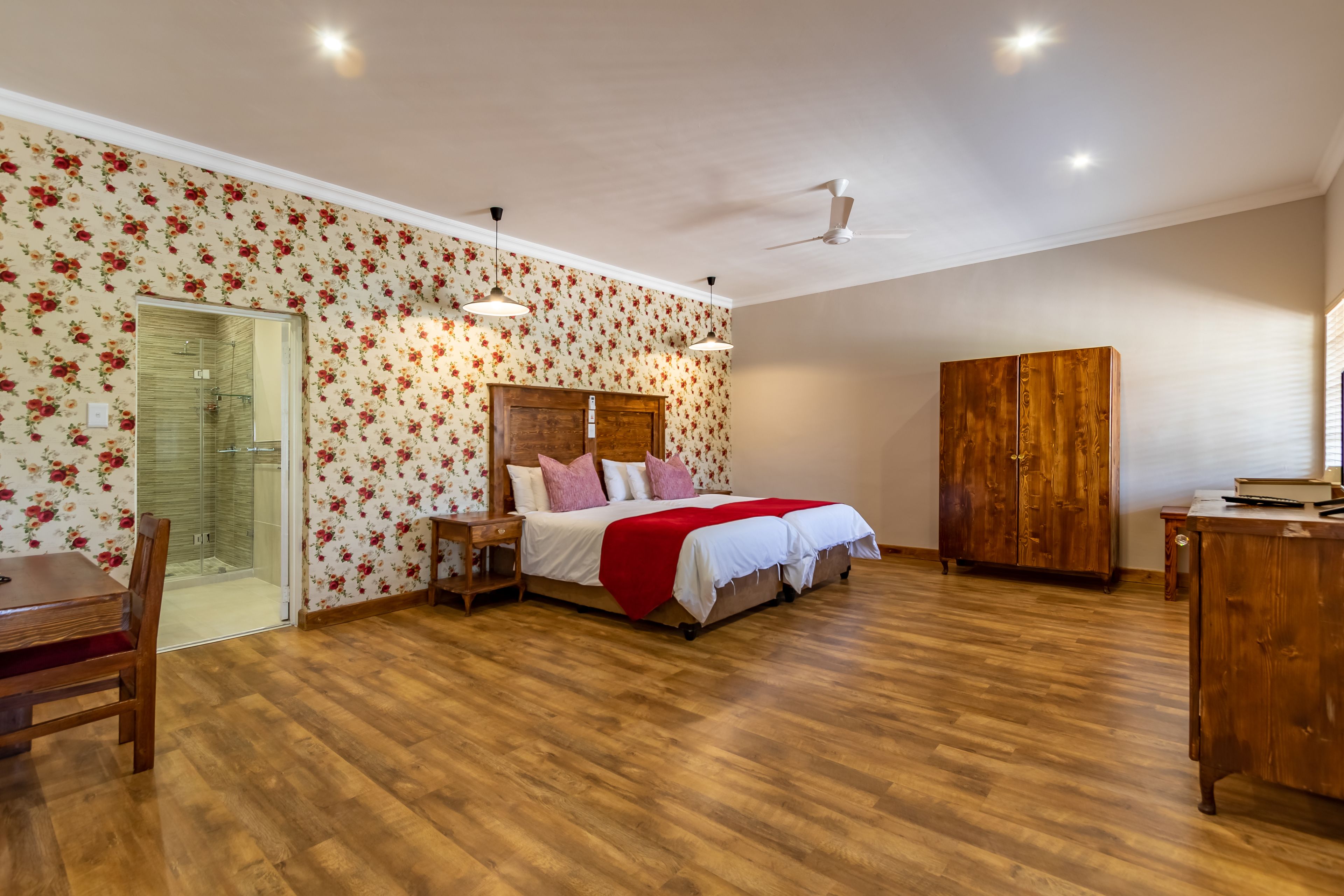 Un dormitorio con piso de madera, una cama con manta roja, un armario y un escritorio con una silla.