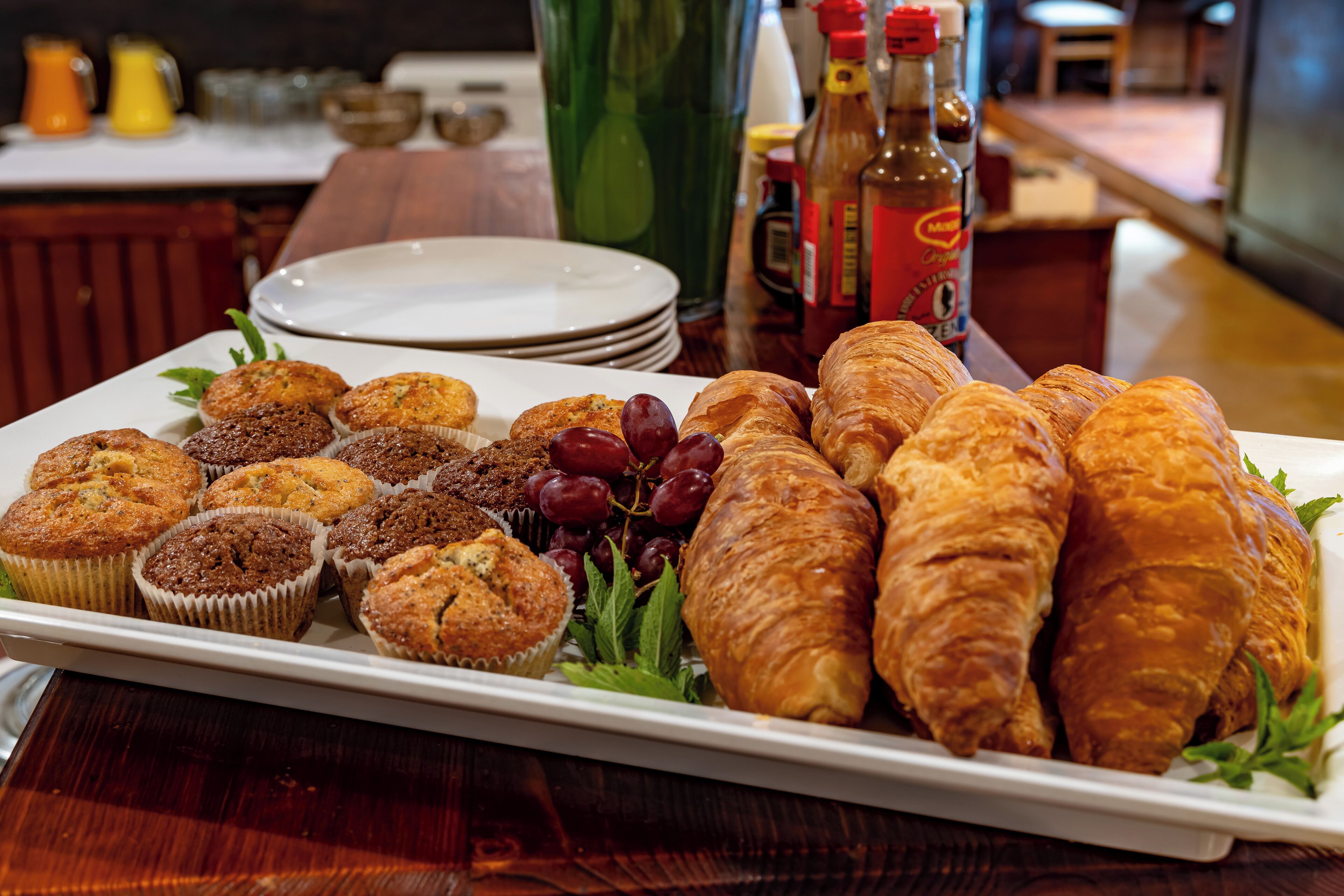 Una bandeja de desayuno con muffins, croissants y uvas sobre un plato blanco.