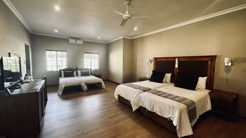 A hotel room with two beds, a desk, a ceiling fan, and a TV.