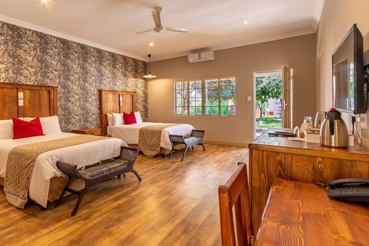 A hotel room with two beds, a desk with a telephone, a chair, and a view of the outdoors.