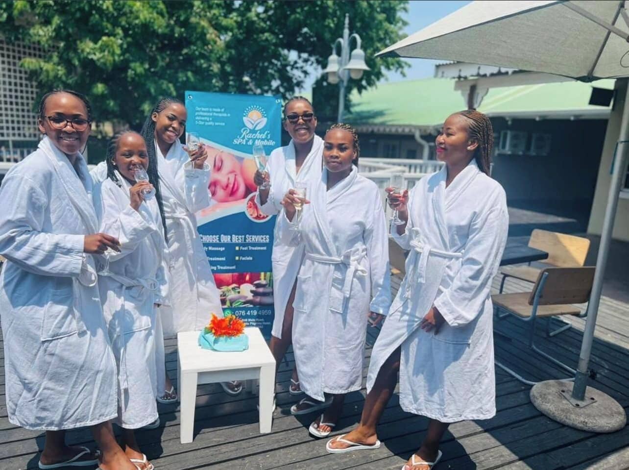 A group of people in white robes standing on a wooden deck with a banner in the background advertising spa services.