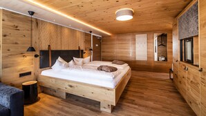 A wooden-paneled bedroom with a bed, bedside tables, and a hanging light fixture. - Alpen Hotel Post**** - Large family nest (Au)