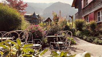 A garden with metal chairs and tables, a wooden structure, and a mountain backdrop.