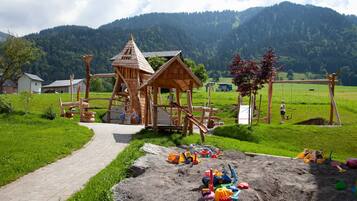 A playground with a wooden play structure, a dirt play area with toys, and a path leading to it.