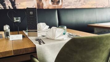 A restaurant setting with a table set for two, a menu, and a wall-mounted painting of a cow.