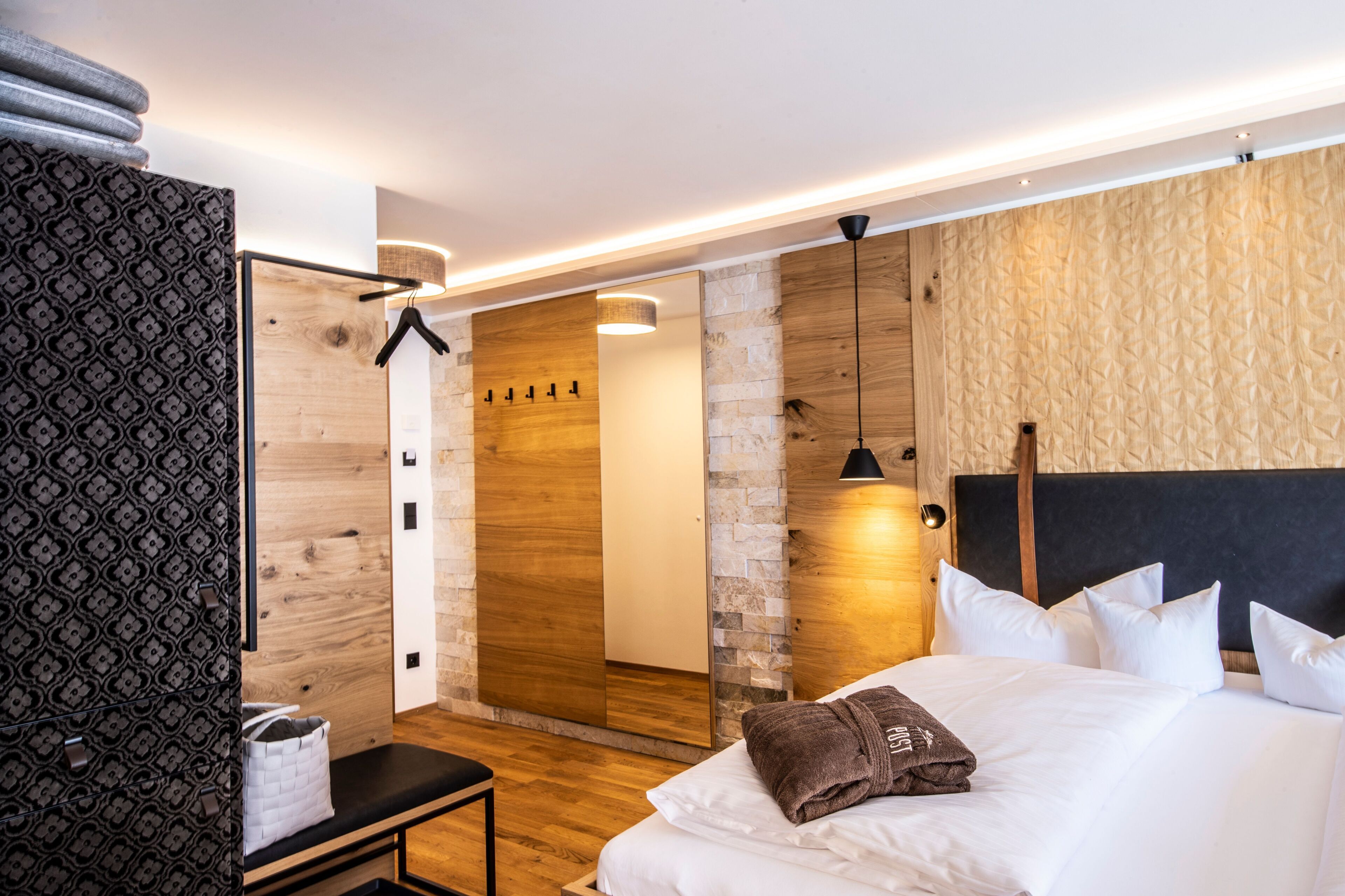 Une chambre d’hôtel moderne avec un grand lit, un banc, un miroir et un mur en bois.
