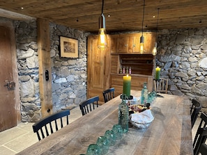 Un comedor rústico con mesa de madera, paredes de piedra y lámparas colgantes.