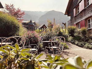 Een tuin met metalen stoelen en tafels, een houten constructie en een berg op de achtergrond.