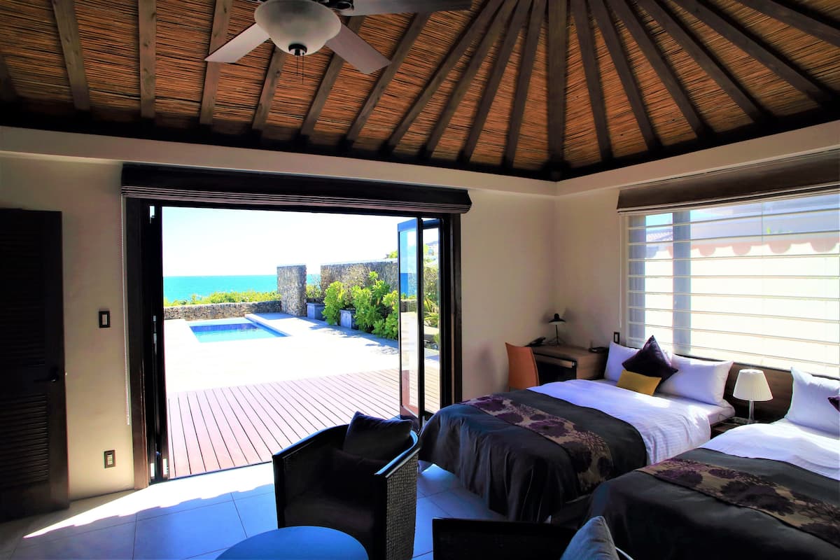 A bedroom with a large sliding glass door leading to a pool area, a ceiling fan, and a bed with multiple pillows.