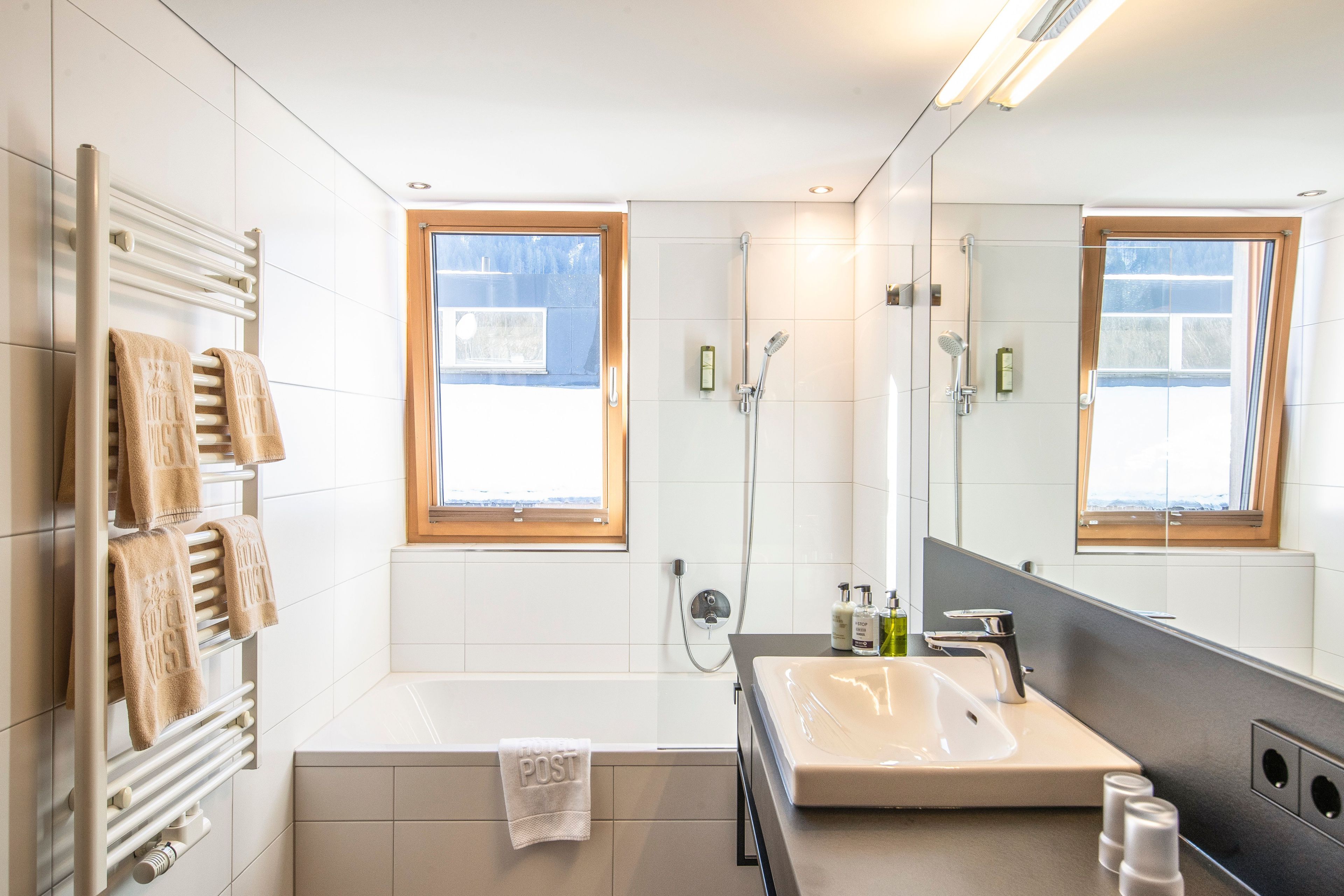 A modern bathroom with a bathtub, a large mirror, and a window.