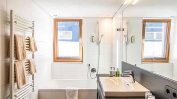 A modern bathroom with a bathtub, a large mirror, and a window.