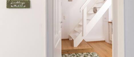 A hallway with a staircase, a green mat with white patterns, and a sign that reads "Lieblings PLATZ".