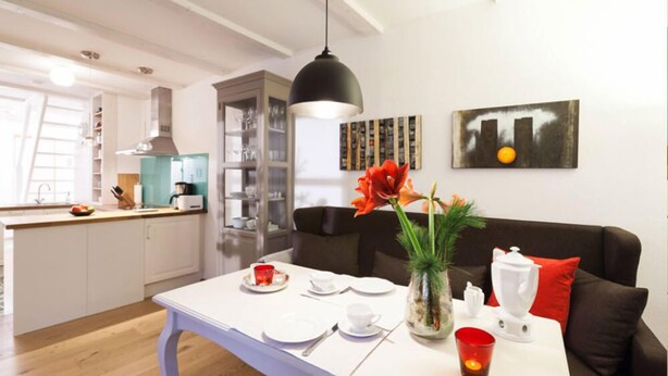A modern kitchen with white cabinets, a dining table set for two, and a black pendant light above. - Ferienwohnung Lieblingsplatz (Lueneburg)